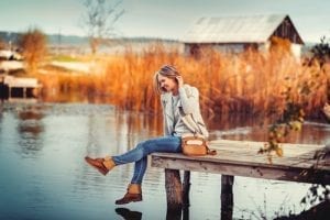 glamourous portrait of the young beautiful woman in leather boots on the bank of a lake on wooden pier